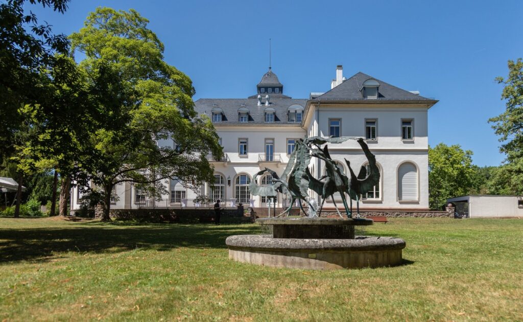 Image of Lichtenberghaus as seen from the Garden with a fountain in the foreground and a tree to the left.