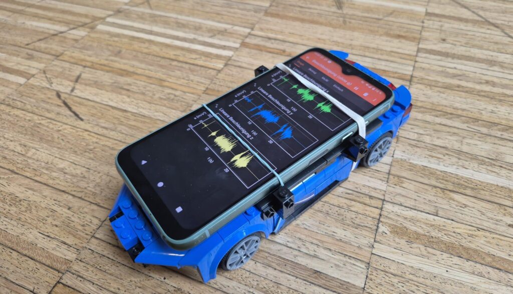Image of the experiment platform - a LEGO "racing car" as base for a smartphone showing measurements in the phyphox app.